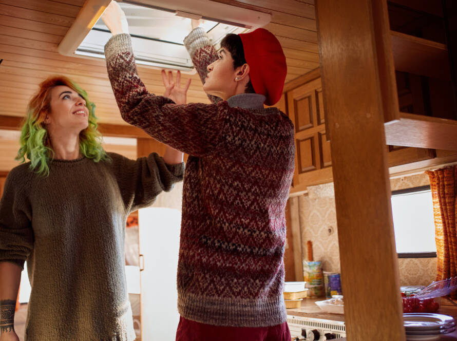 Two friends fixing roof window inside of camper trailer.