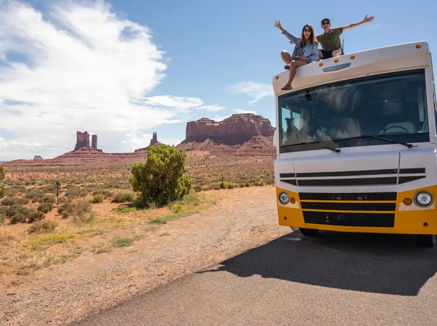 Young couple on top of RV celebrating a road trip.